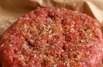 hamburger seasoning being sprinkled on a raw hamburger patty