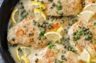 a skillet of chicken piccata garnished with lemon slices
