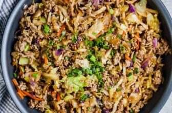a skillet of egg roll in a bowl garnished with green onions and sesame seeds