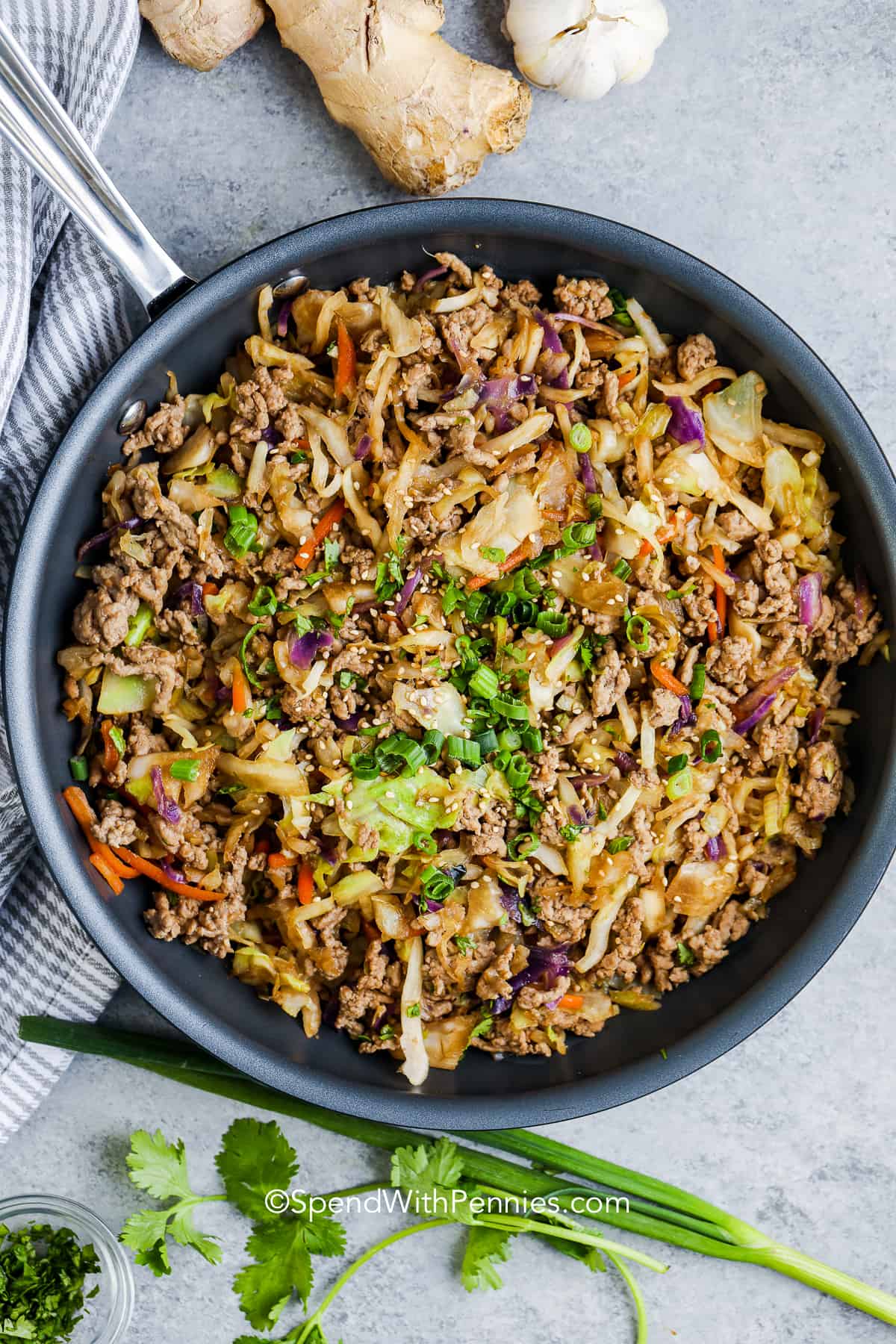 a skillet of egg roll in a bowl garnished with green onions and sesame seeds