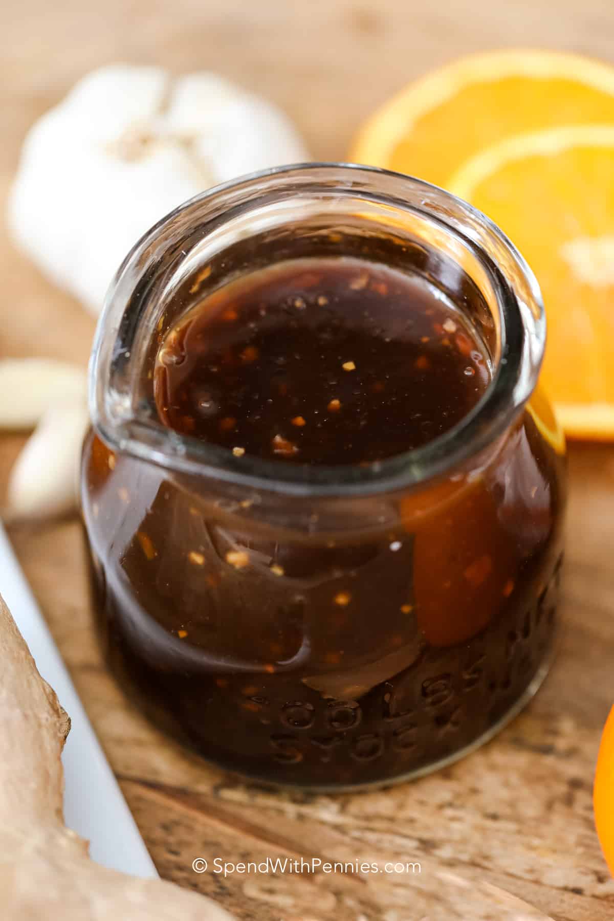 a jar of teriyaki sauce next to orange slices and garlic