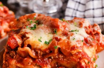 Crock pot lasagna on a plate with garlic bread in a basket.