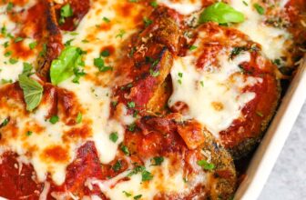 eggplant parmesan in a white dish with fresh basil as garnish