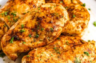 4 air fryer chicken breasts on a plate with green beans in the background