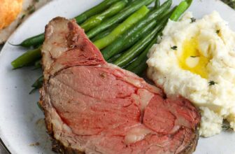 a slice of prime rib with mashed potatoes and green beans on a plate